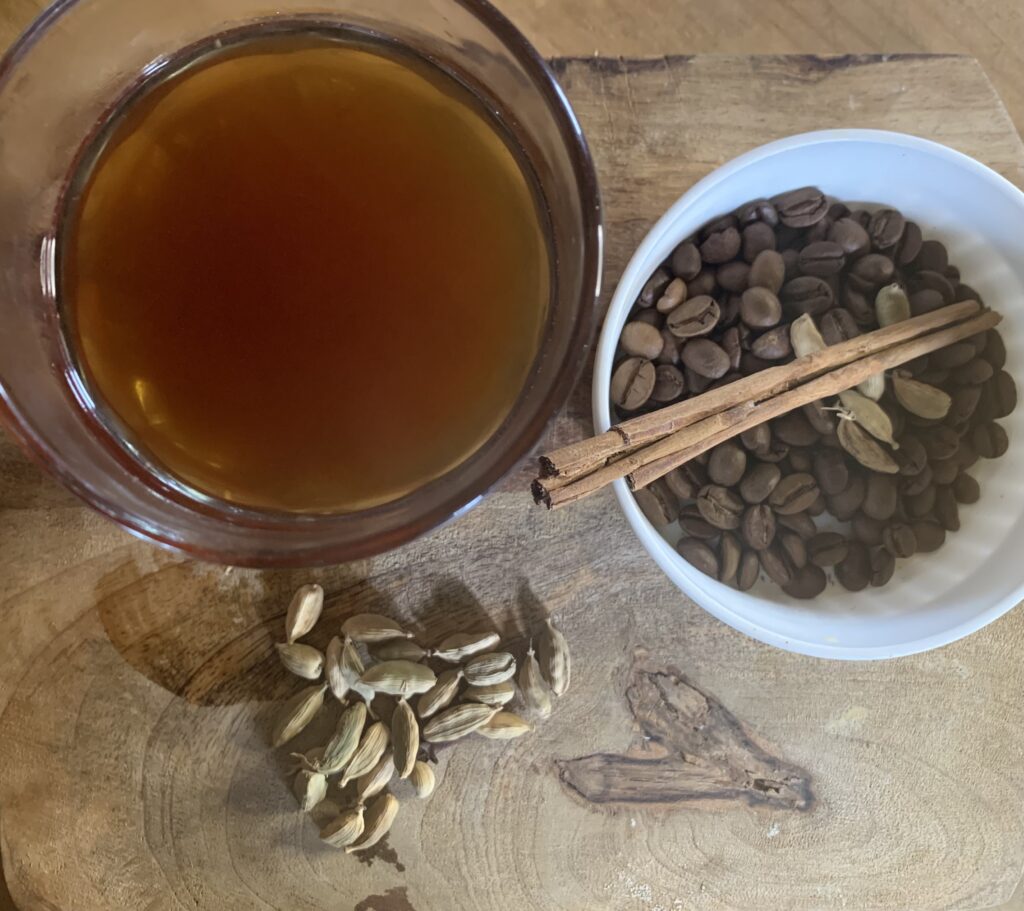 un vaso con café sobre una mesa de madera junto a semillas de cardamomo granos de café Y un palo de canela